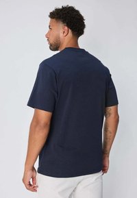 T-shirt à manches courtes bleu marine en coton, avec un col rond et une coupe décontractée. Le dos présente un design uni sans logo visible.