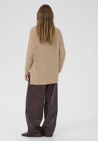 Beige ribbad tröja med långa ärmar, kombinerad med oversize mörkbruna läderbyxor. Löst snitt, sidöppningar vid tröjans nederkant.