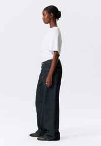 Loose-fitting dark blue denim jeans with visible stitching and side pockets, paired with a plain white short-sleeve t-shirt.