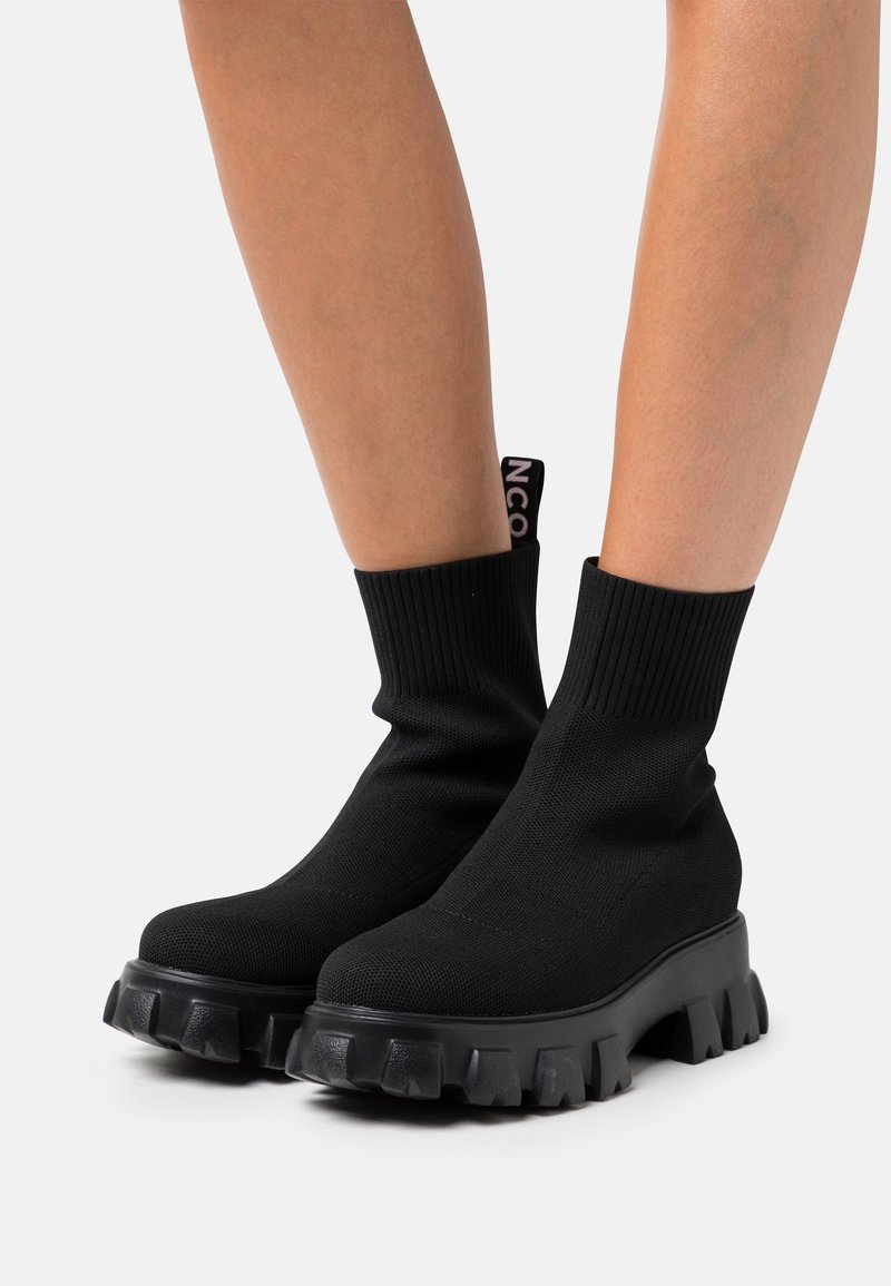 Bottes de cheville en tricot noir avec un col côtelé, semelle texturée épaisse et détail de logo à l'arrière. Finition lisse avec un design montante.
