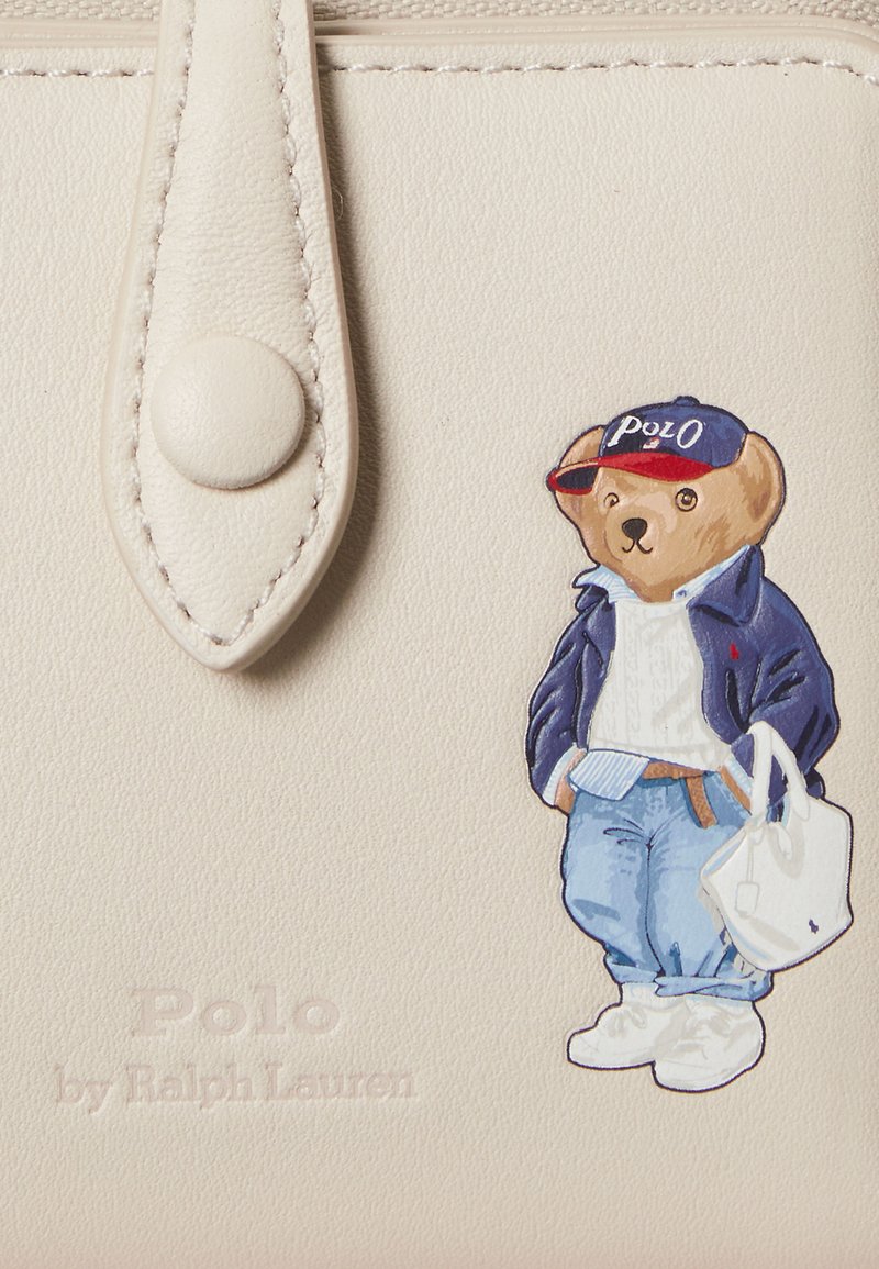 Cremefarbenes Leder mit einer bunten Illustration eines Bären, der eine blaue Jacke und Mütze trägt und eine weiße Tasche hält. "Polo by Ralph Lauren" geprägt.