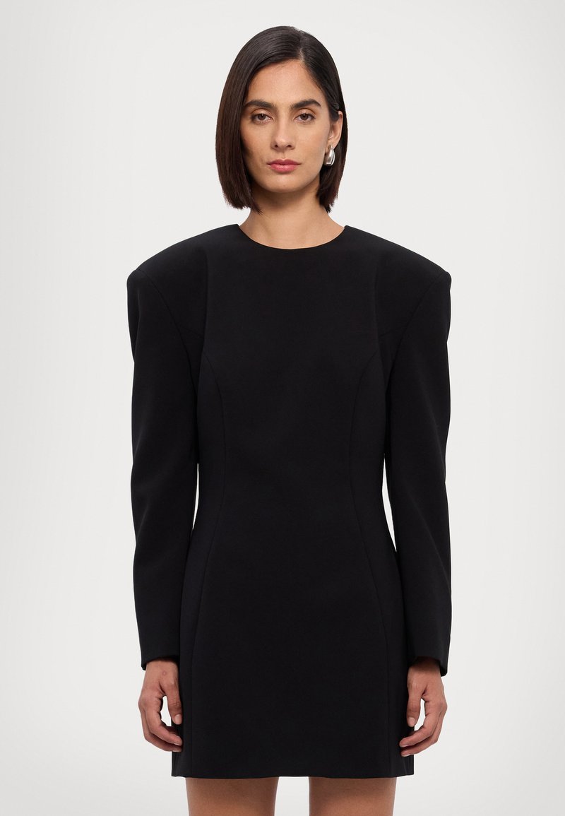 Robe noire à manches longues avec des épaules structurées, un corsage ajusté et une jupe droite. Fabriquée dans un tissu lisse et mat.