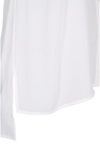 Tissu blanc à la texture lisse, présentant une petite fente latérale et un ourlet courbé, montré en gros plan.