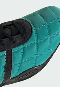 Teal quiltet sneaker med en sort ruskind tåhætte, sorte snørebånd og struktureret gummisål med brandingdetalje.