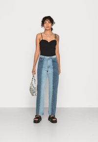 Jeans de ganga largos azuis com painéis contrastantes claros e escuros, combinados com uma camiseta preta ajustada e acessorizados com uma bolsa com padrão de zebra.