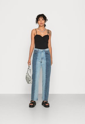 Jeans de ganga largos azuis com painéis contrastantes claros e escuros, combinados com uma camiseta preta ajustada e acessorizados com uma bolsa com padrão de zebra.
