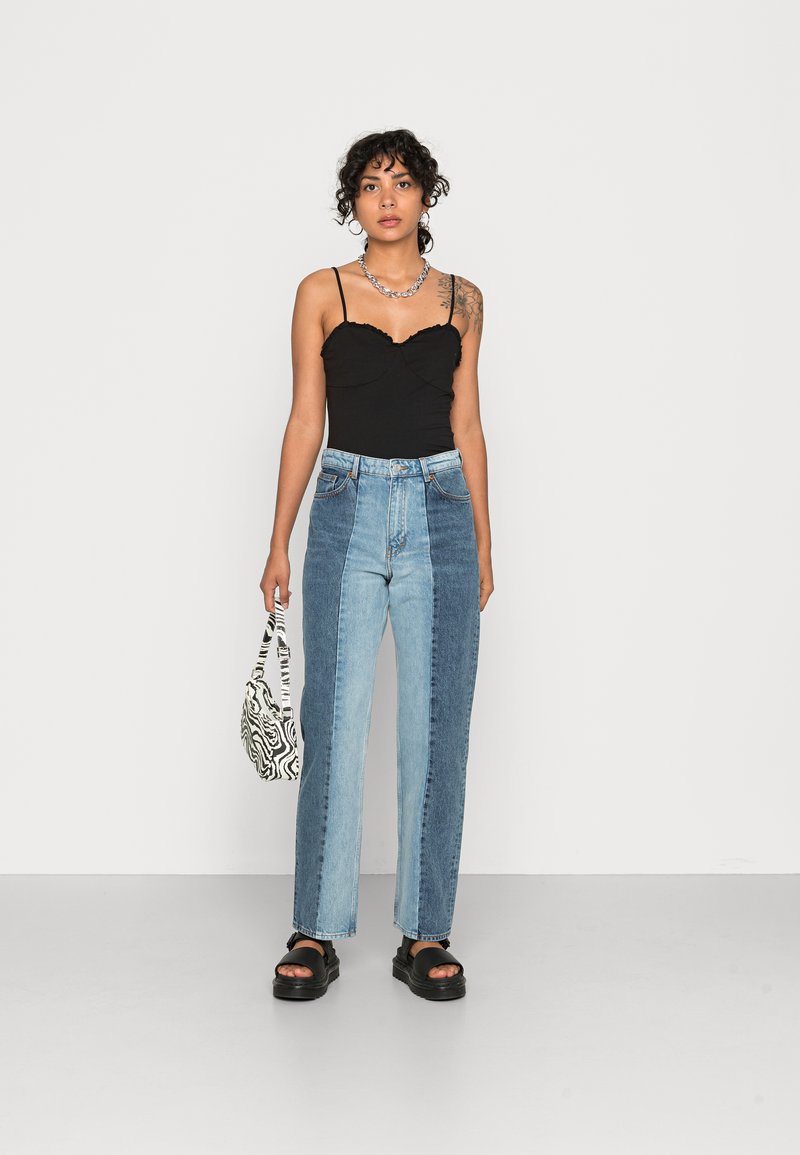 Jeans de ganga largos azuis com painéis contrastantes claros e escuros, combinados com uma camiseta preta ajustada e acessorizados com uma bolsa com padrão de zebra.