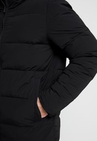 Sort pufferjakke med vandret syninger, lynlås lukning og sidelommer. Lavet af glat, isoleret stof. Enkel design uden mønstre.