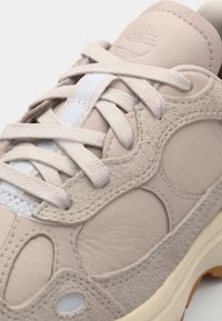 Ljusbeige sneakers med en strukturerad läderutsida, runda utskärningar och platta snörningar. Har en gummisula med lätt upphöjning.