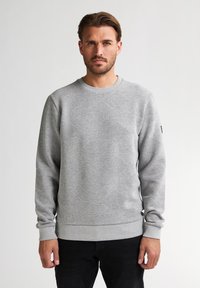 Grijze sweatshirt met een getextureerd ruitpatroon, geribde manchetten en een ronde halslijn. Gecombineerd met zwarte broeken voor een casual look.