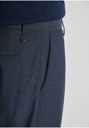 Primer plano de pantalones de vestir azul marino con un sutil patrón de puntos y un detalle de presilla a juego en una persona que lleva un top azul oscuro.