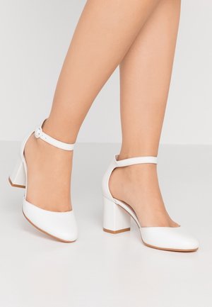 Białe lakierowane skórzane szpilki z okrągłym noskiem, paskiem na kostce i blokowym obcasem, charakteryzujące się gładką powierzchnią i minimalnymi ozdobami.