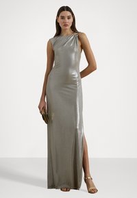 Rochie metalizată argintie, fără mâneci, cu detalii drapate la umăr, fanta până la coapsă și textură netedă, asortată cu o poșetă aurie și sandale.
