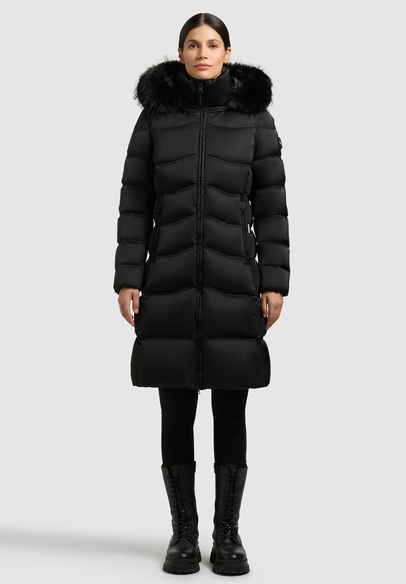 Mustast õhukindlast materjalist talvejope eemaldatava karvaga kapuutsiga, tikandiga, ees tõmblukk ja küljetaskud, kombineeritud mustade retuuside ja paeltega saapadega.