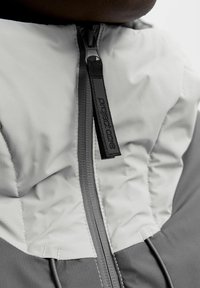 Reißverschlussjacke mit einem zweifarbigen Design in Grau und Hellgrau. Hergestellt aus strukturiertem Stoff mit sichtbaren Nähten und einem markierten Reißverschlussanhänger.