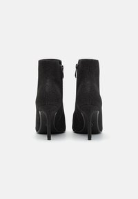 Botines negros con un acabado elegante y texturizado, altos tacones de aguja y cierre de cremallera en el lateral, que presentan un diseño de curva suave.