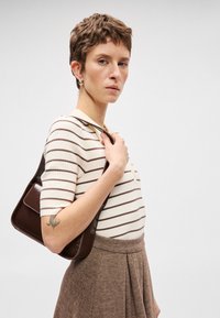 Καφέ και κρέμα ριγέ κοντομάνικο πουλόβερ σε συνδυασμό με καφέ φούστα σε σχέδιο καρό. Μία μικρή καφέ τσάντα κρεμάται στον ώμο.