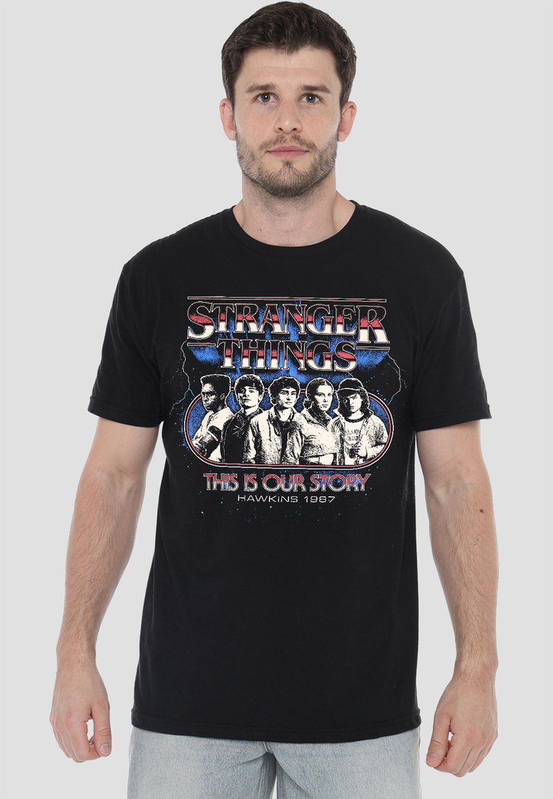 Schwarzes Baumwoll-T-Shirt mit einem Grafikdesign von Charakteren und dem Text "STRANGER THINGS - DAS IST UNSERE GESCHICHTE - HAWKINS 1987" in lebendigen Farben.