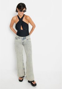 Fato de banho preto com alças à halter, frente drapeada e detalhe em forma de buraco, combinado com jeans azuis claros de corte fluido com um acabamento desbotado e grandes bolsos.