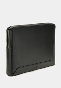 Czarna, syntetyczna osłona na laptopa o gładkiej fakturze, zamykana na zamek, z akcentem logo na dole. Prostokątny kształt z zaokrąglonymi rogami.