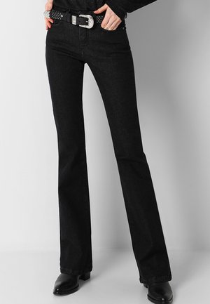 Black flared jeans with a smooth texture, waistband with belt loops, and a silver buckle. Paired with black ankle boots.