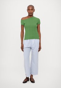 Top verde cu umeri descoperiți, asortat cu pantaloni lejeri cu dungi albastre și albe. Topul are un design ajustat, în timp ce pantalonii au o croială dreaptă.