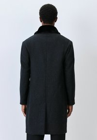 Tmavošedý kabát s textúrovaným vzorom, ktorý má čierny golier. Prispôsobený dizajn, dlhé rukávy a stredná dĺžka.