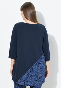 Tunic navy con design diagonale: parte superiore blu navy uniforme e sezione inferiore a motivo blu. Tessuto morbido; maniche a 3/4.