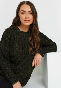 Pull en tricot épais vert foncé avec un col rond et des manches longues, présentant un motif texturé et des poignets côtelés.