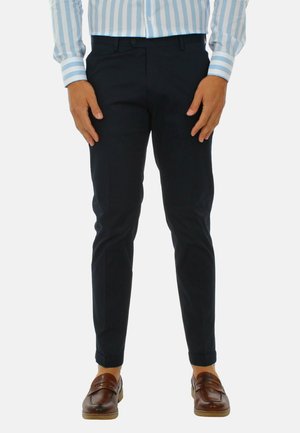 Pantaloni navy con una vestibilità su misura, realizzati in tessuto morbido. Presentano una parte anteriore piatta e gambe affusolate. Indossati con mocassini marroni.
