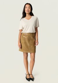 Beige V-neck t-paita yhdistettynä ruskeaan nahkaminihameeseen, jossa on kaksi etutaskua. Mallilla on jalassaan mustat kärjelliset ballerinat.