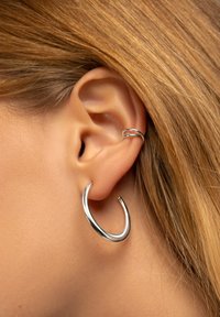 Pendiente de aro de plata con un acabado suave y pulido, que presenta un diseño minimalista de abertura. Un segundo aro metálico también se lleva más alto en la oreja.