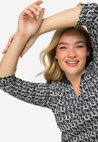 Blusa navy con un motivo geometrico in crema, presenta un collo a V e polsini verdi lime con bordi ondulati, realizzata in un tessuto leggero.