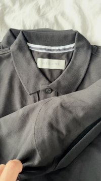Polo negro con cuello abotonado, hecho de una tela texturizada. Presenta una etiqueta con la marca "PIER-ONE" y rayas horizontales debajo del cuello.
