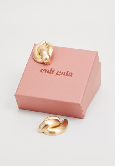 Gouden kettingoorbellen met een gladde, glanzende textuur, weergegeven naast een roze doos met de tekst "cult gaia" in bruine letters.