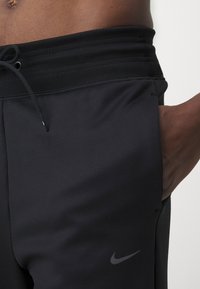 Sorte treningsbukser med elastisk midje, snor detalj og sidelomme. Har en subtil grå Nike-logo. Glatt tekstur.