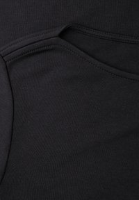 Sort stof med en glat tekstur, der har en buet søm og en lommeåbning. Materialet ser ud til at være strækbart og tætsiddende.