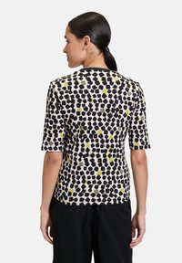 Koszulka z krótkim rękawem z teksturowanego materiału, z czarno-żółto-zielonym abstrakcyjnym nadrukiem na kremowym tle, z prostym, okrągłym dekoltem.