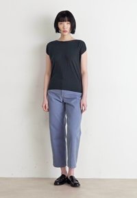 Top preto de manga curta com um corte descontraído, combinado com calças azul claro, ligeiramente ajustadas, e mocassins pretos. Design simples, textura suave.