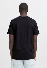 Svart t-skjorte med korte ermer og rund hals, laget av mykt stoff. Glatt tekstur med en avslappet passform, kombinert med lyseblå jeans.