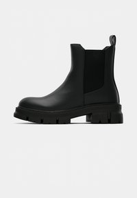 Čierna kožená Chelsea obuv s robustnou podrážkou, elastickou bočnou časťou, pútkom na zadnej strane a nízkym opätkom, zobrazená zo strany na bielom pozadí.