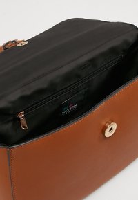 Hnědá kožená kabelka s černou látkovou vnitřní částí, která má zipovou kapsu a zlaté magnetické zapínání.