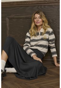 Stribet langærmet top i beige og sort, med et broderet NYC-logo, parret med en sort maxinederdel og hvide sokker.