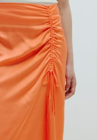 Orange Satinrock mit seitlicher Raffung und gebundenem Akzentdetail. Verfügt über eine glatte Textur und eine fließende Silhouette.