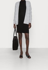 Grå stickad cardigan med strukturerat mönster, bärs över en figurnära svart ribbad klänning. En svart mocka-väska och öppna klacksandaler fulländar stilen.