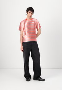 Tricou cu mânecă scurtă, dungat roșu și alb, cu gât rotund, asortat cu blugi negri cu picioare largi și pantofi negri.
