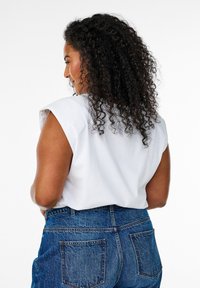 Vit ärmlös topp med strukturerade axlar, i kombination med högmidjade blå denimjeans med bakfickor och en klassisk passform.