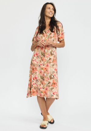 Blomster midi kjole med en blanding af pink og beige farver, korte puffærmer og en løs, svævende pasform. Båret med flade sandaler.