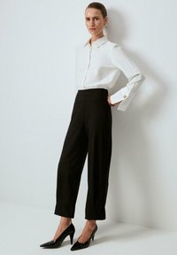 White button-up shirt with a pointed collar, black high-waisted trousers, and black pointed-toe heels. Smooth fabric and tailored fit.