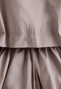 Tissu beige avec un détail de cordon froncé et un logo métallique "aim'n le Run" cousu près de la couture.